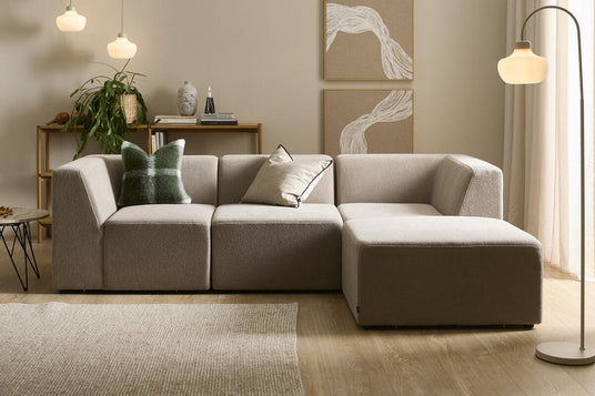 Beige modulsoffa i ljus skandinavisk vardagsrumsmiljö med golvlampa, tre pendlar, väggkonst, matta och grön växt.
