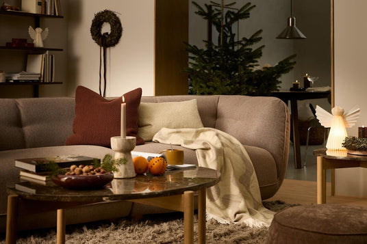 Vardagsrum med brun soffa, julgran, tända ljus, kuddar och pläd på soffan; varm och mysig julstämning.