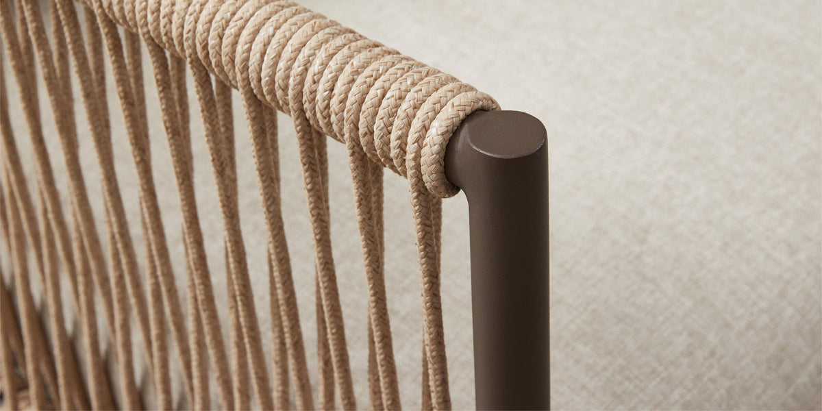 Närbild av flätad repdetalj runt brunt metallarmstöd med beige klädsel i bakgrunden.