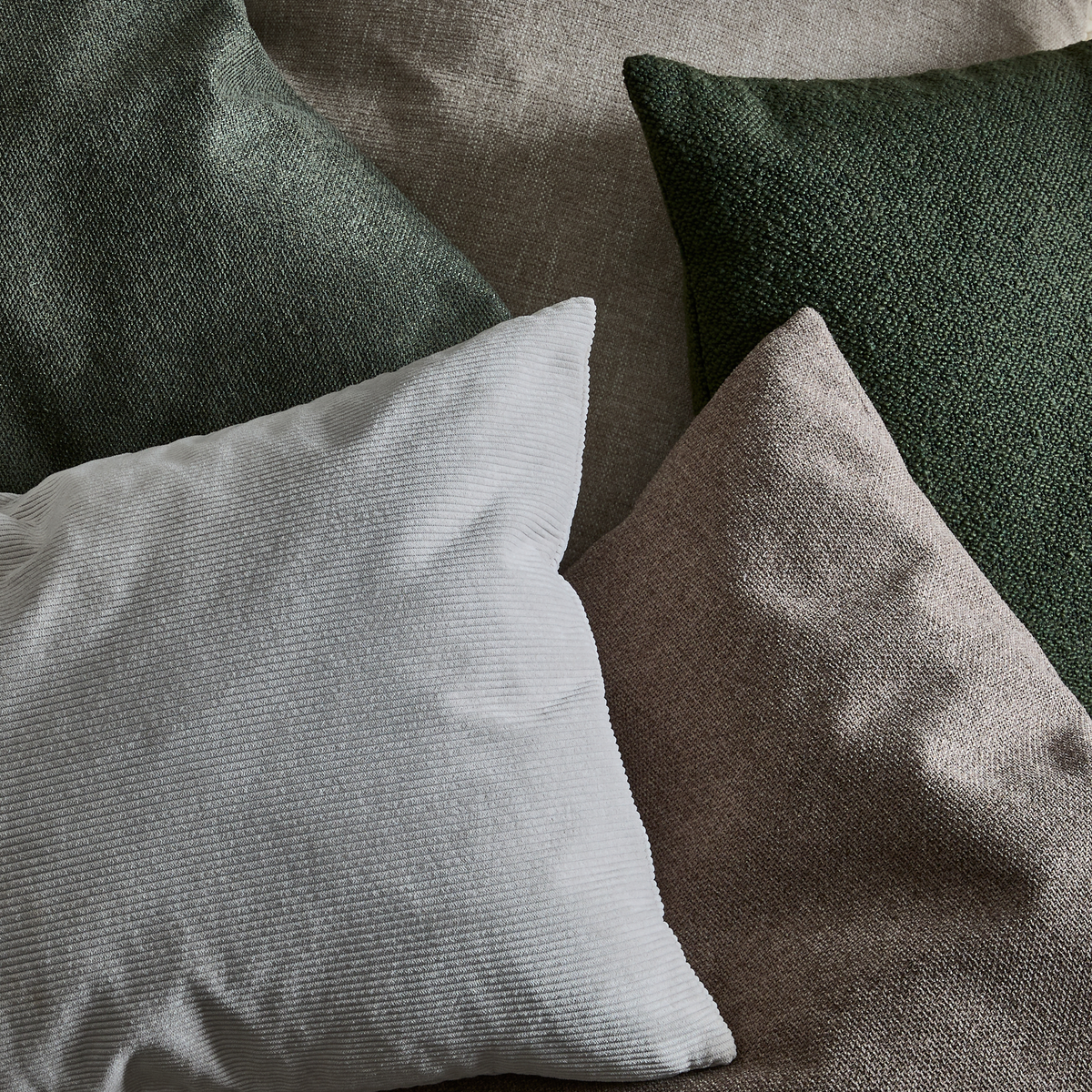 Närbild av flera prydnadskuddar i mörkgrönt, beige och vitt med tydliga texturer.