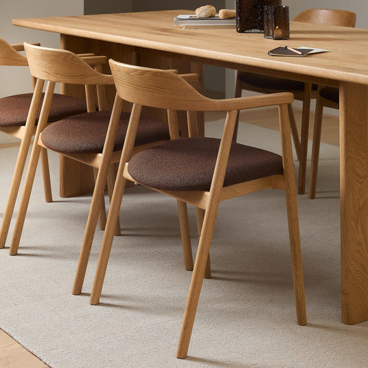 Närbild av ekstolar med brun klädd sits kring ett ekbord på en ljus matta i en minimalistisk matsal.