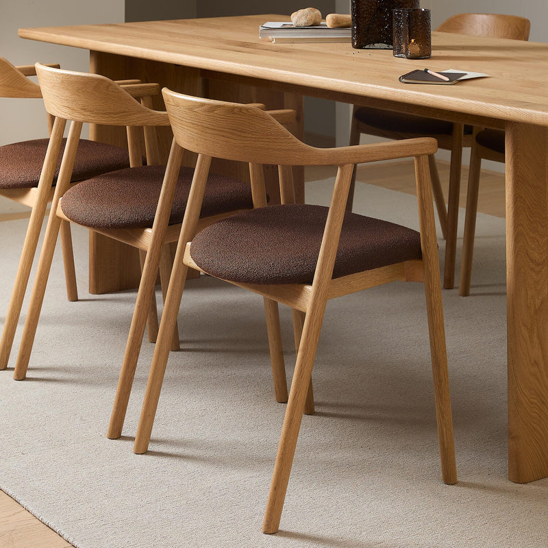 Närbild av ekstolar med brun klädd sits kring ett ekbord på en ljus matta i en minimalistisk matsal.