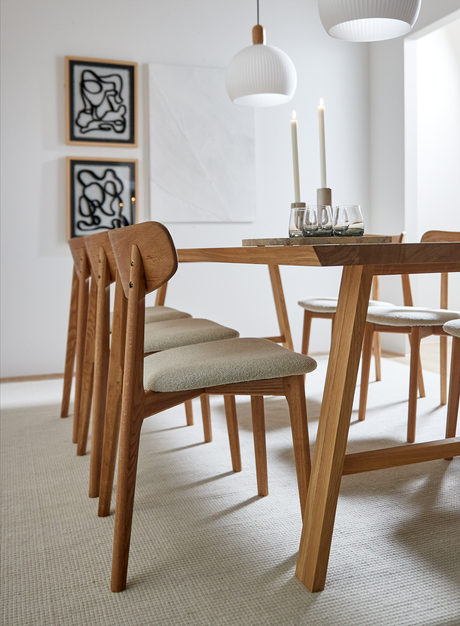 Ljust matrum med ekbord och stoppade trästolar, två vita pendellampor och tända ljus på bordet i neutral skandinavisk stil.