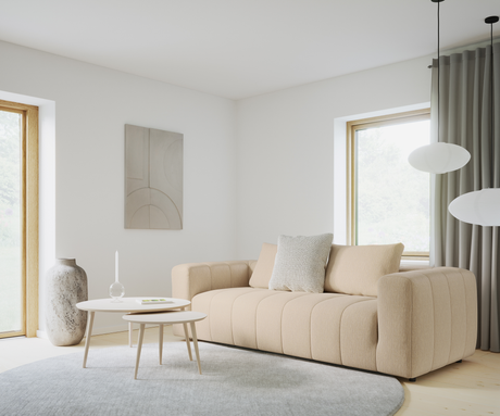 Ljus skandinavisk vardagsrumsinteriör med beige soffa, två runda vita soffbord med ljus och glasdekoration, stor grå rund matta, stenvase, abstrakt väggkonst samt rispapperspendlar vid fönster med grå gardiner.