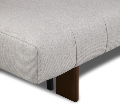 Närbild av ett ljusbeige, kanalstickat stoppat bänk/soffhörn med mörkt träben mot svart bakgrund.