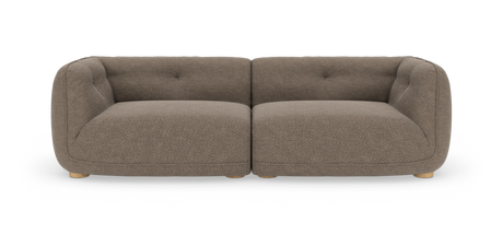 Framifrån vy av en tvåsitsig, modulär soffa i taupe bouclé med rundade armstöd och låga träfötter, frilagd mot vit studiobakgrund.