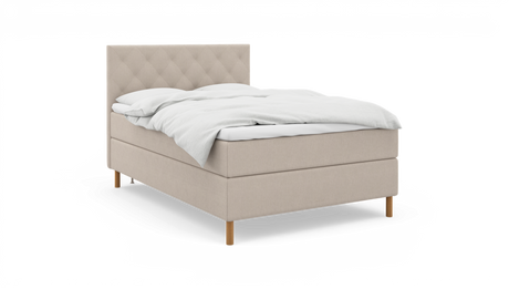 Beige kontinentalsäng med quiltad sänggavel, trärben och vit bäddning, frilagd.