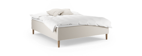 Beige säng med träben och vit bäddning, två kuddar och en fluffig täcke, frilagd på svart bakgrund.