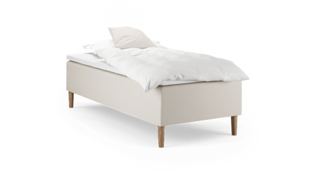 Enkelbädd med beige klädd sängbas, träben och vit bäddning med kudde.