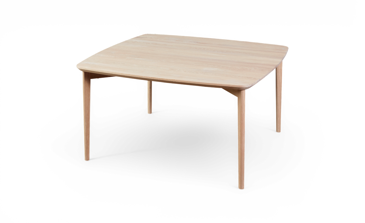 Ljus ekfärgat fyrkantigt matbord med rundade hörn och smala ben, frilagt på vit bakgrund.