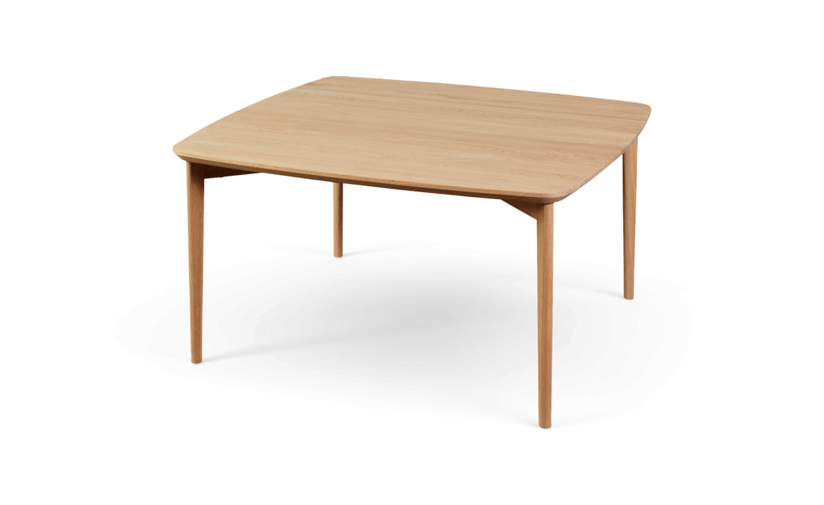 Ljus ekfärgat kvadratiskt matbord med mjukt rundade hörn och avsmalnande ben.