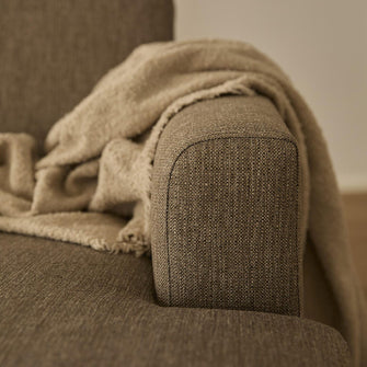 Närbild på soffans armstöd i beige textil med en mjuk beige pläd draperad över.