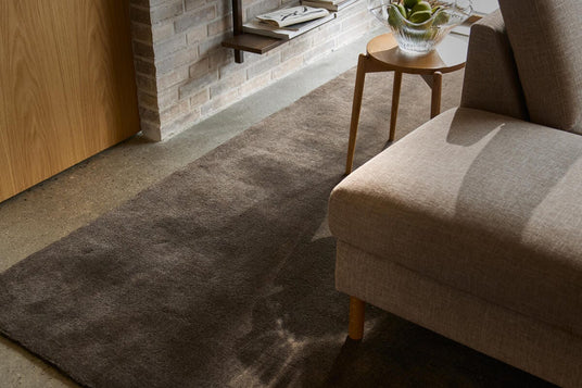 Mörk avlång matta i ett vardagsrum med beige soffa och litet träbord med glasskål med gröna äpplen i mjukt dagsljus.