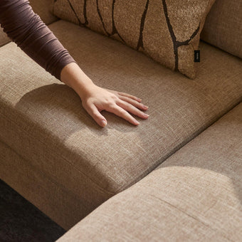 Hand som trycker på beige tygsoffa; IKEA-etikett på kudden syns i varmt solljus.