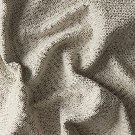Närbild av beige bouclétyg med mjuk, knoppig struktur och veck.