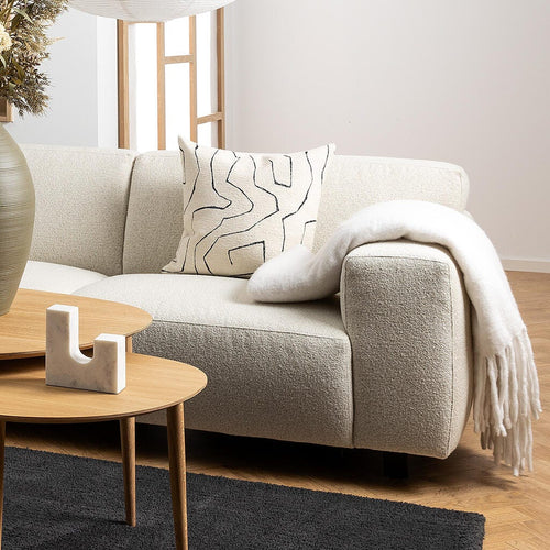 Ljust skandinaviskt vardagsrum med beige hörnsoffa, runda soffbord i trä på svart matta och två stora rislampor; stor vas med torkade växter och grafiskt mönstrad kudde.