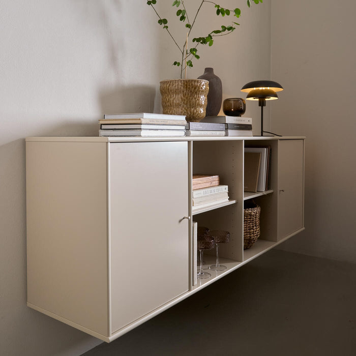 Beige väggmonterad förvaringsmöbel med öppna hyllor, böcker, bordslampa och kruka med grön kvist.