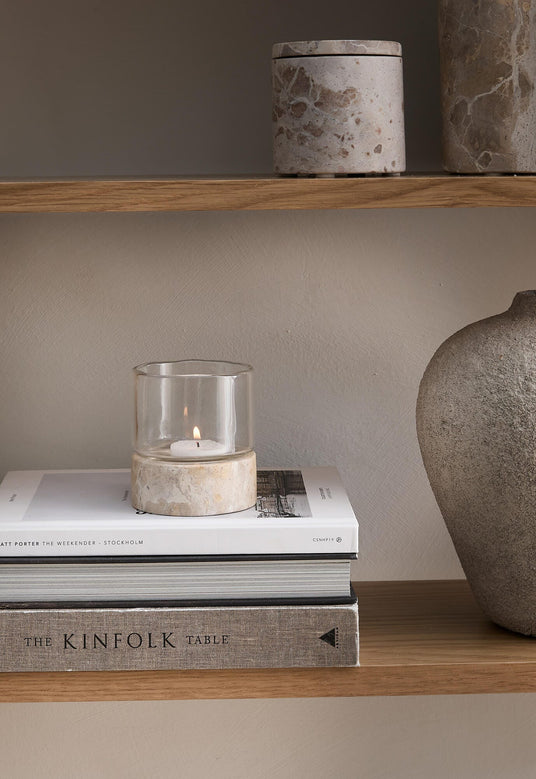 Hylla med ljuslykta i glas på stenfot ovanpå böckerna ”The Weekender – Stockholm” och ”The Kinfolk Table”, bredvid en stenvas.