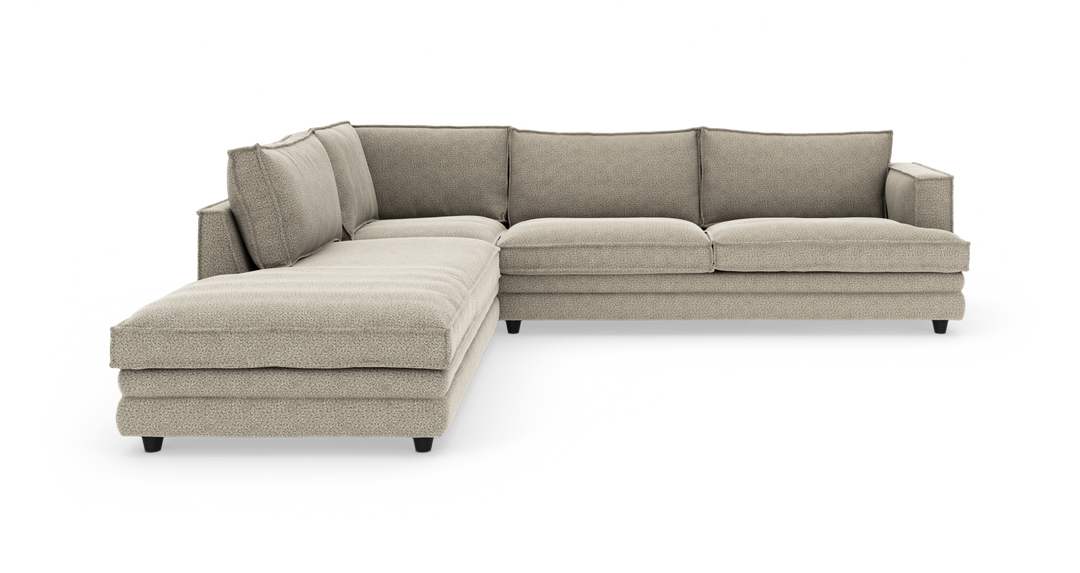 Beige L-formad modulsoffa med vänsterställd schäslong, tjocka sittdynor och lösa ryggkuddar på svarta ben.