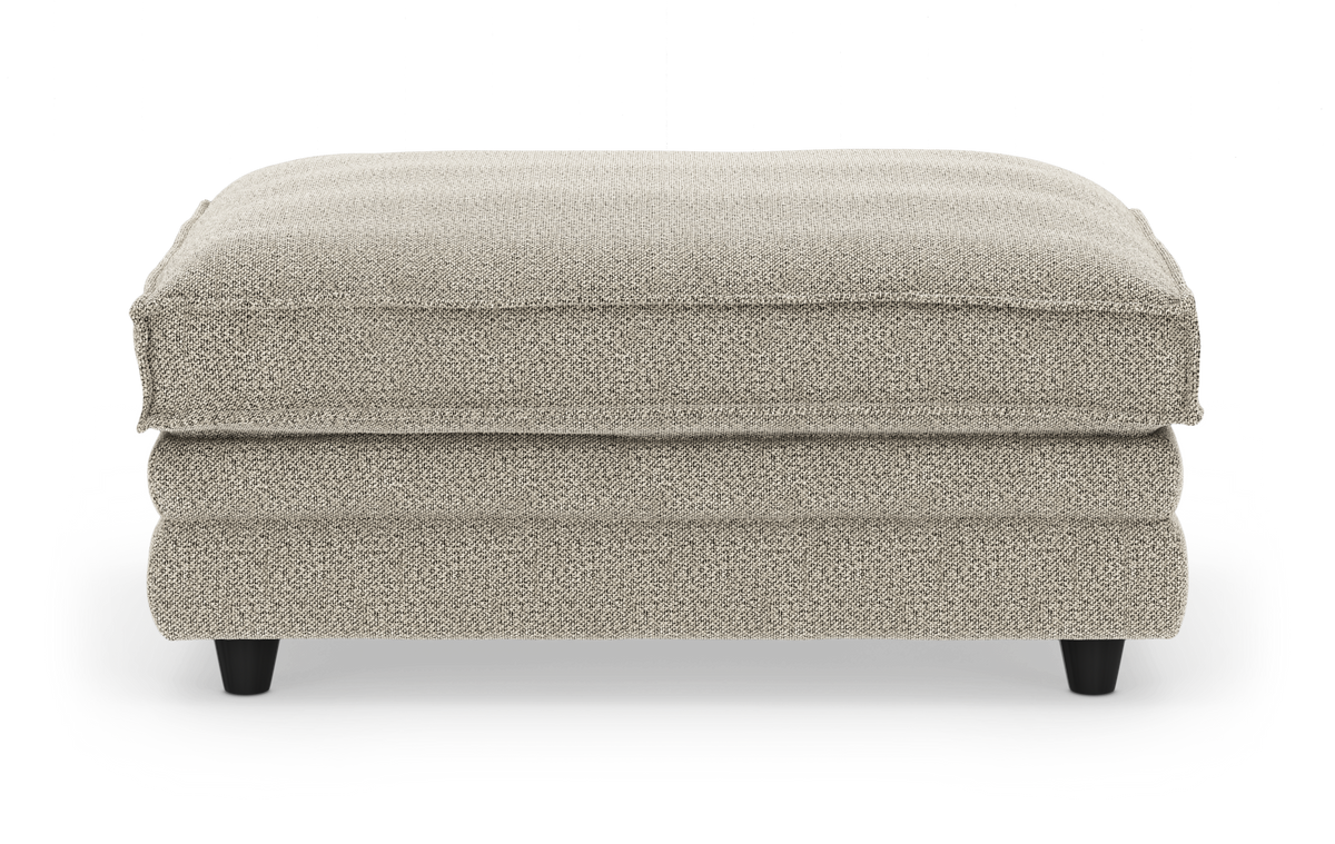 Beige tygpall/ottoman i studiomiljö sedd framifrån.