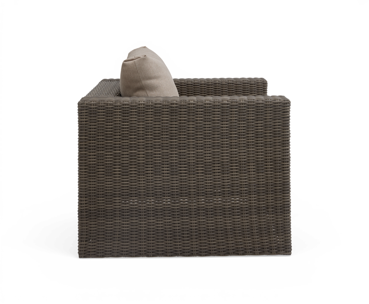 Sidovy av brun rottingfåtölj med beige kudde, frilagd mot vit bakgrund.