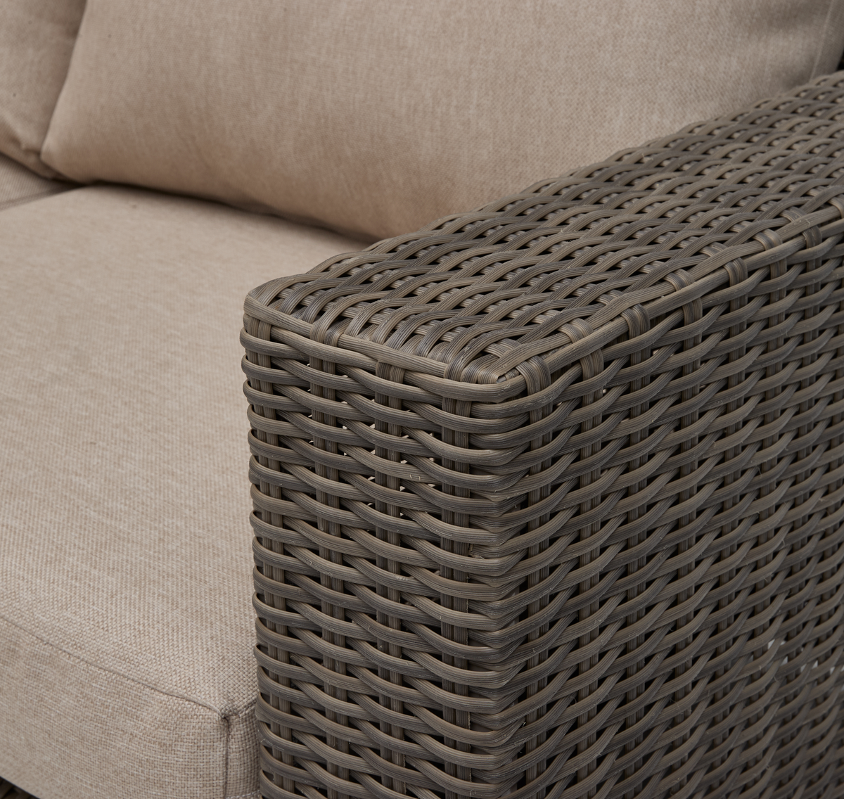 Närbild på armlän i brungrå konstrotting med beige soffkuddar.