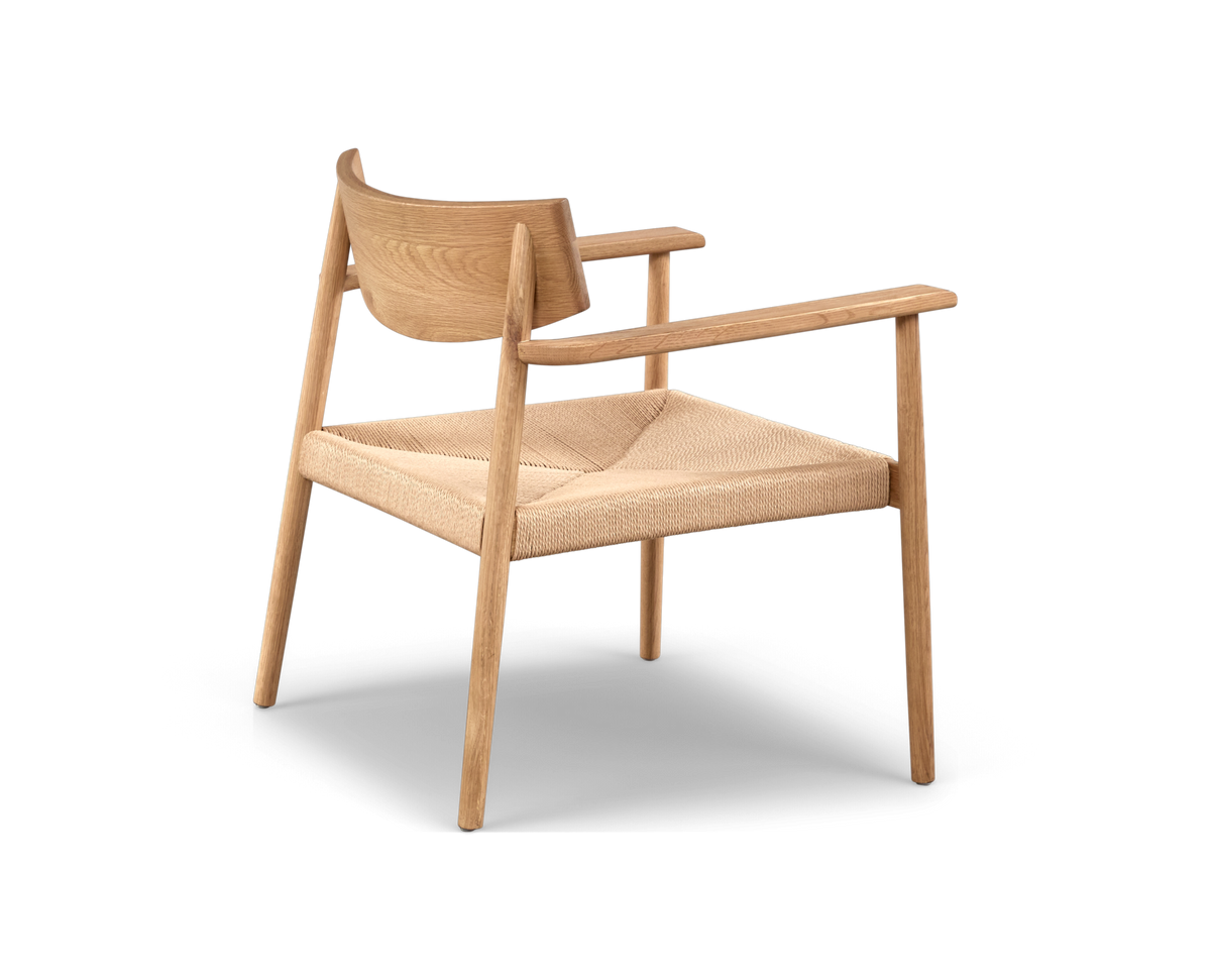 Minimalistisk armstol i ljust trä med flätad sits, sedd snett bakifrån på vit bakgrund.