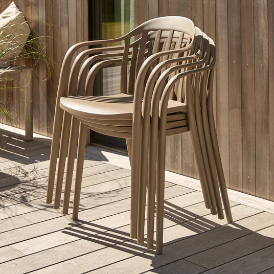 Staplade beige utestolar på en träterrass i solljus.