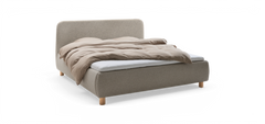 Polstrad säng med rundad huvudgavel i ljusgrå textil, beige täcke och ljusa träben.