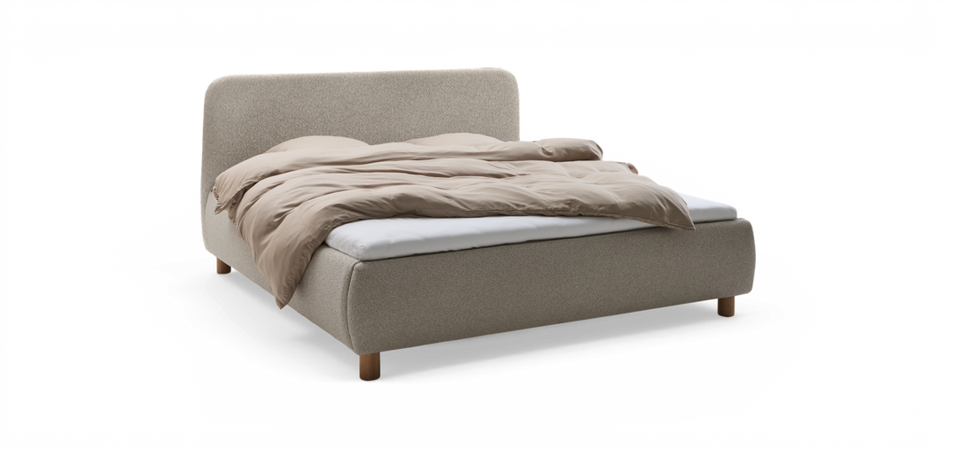 Uppklädd säng med rundad huvudgavel i ljus textil, beige täcke och synliga träben, fotad snett framifrån på neutral bakgrund.