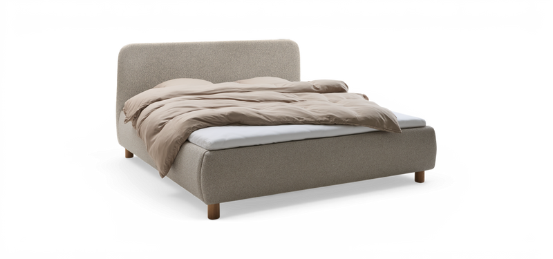 Uppklädd säng med rundad huvudgavel i ljus textil, beige täcke och synliga träben, fotad snett framifrån på neutral bakgrund._ps