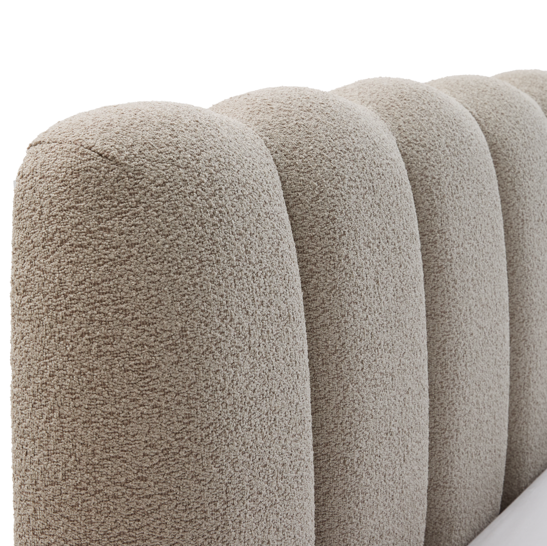 Närbild av rundad, kanalquiltad sänggavel i beige bouclé.