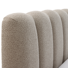 Närbild av rundad, kanalquiltad sänggavel i beige bouclé.