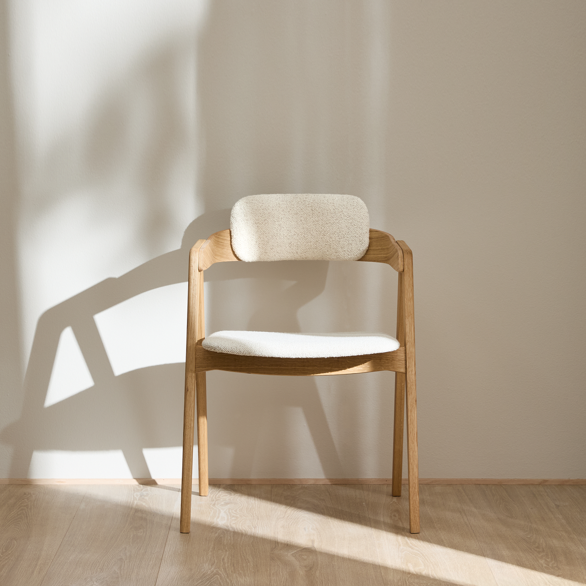 Ljus trästol med ljus stoppad sits och rygg mot beige vägg i mjukt dagsljus.