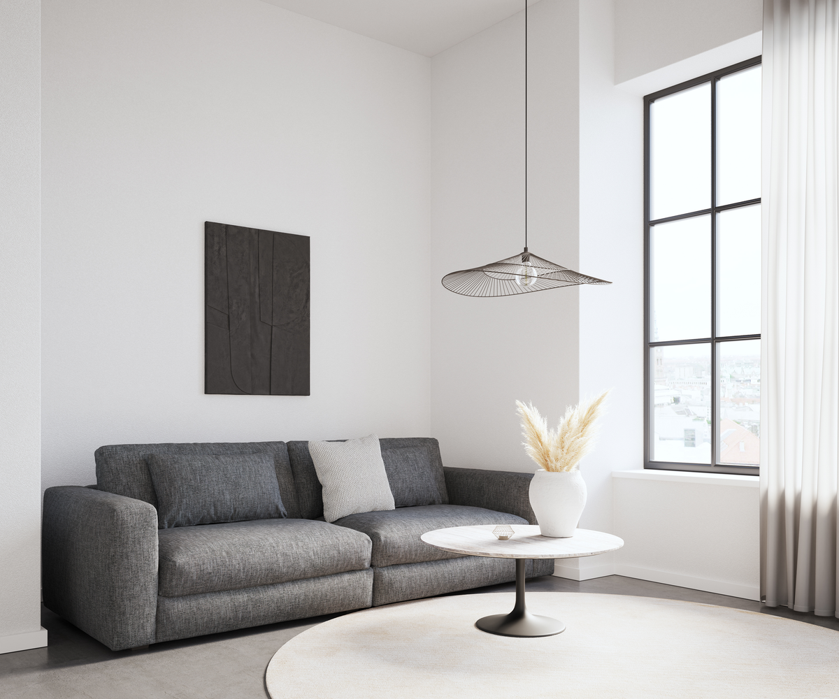 Ljus skandinavisk vardagsrumshörna med grå soffa, runt soffbord i marmor-look, vit vas med pampasgräs, stort svartspröjsat fönster och luftig trådpendel.