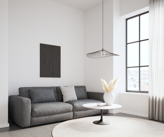 Ljus skandinavisk vardagsrumshörna med grå soffa, runt soffbord i marmor-look, vit vas med pampasgräs, stort svartspröjsat fönster och luftig trådpendel.
