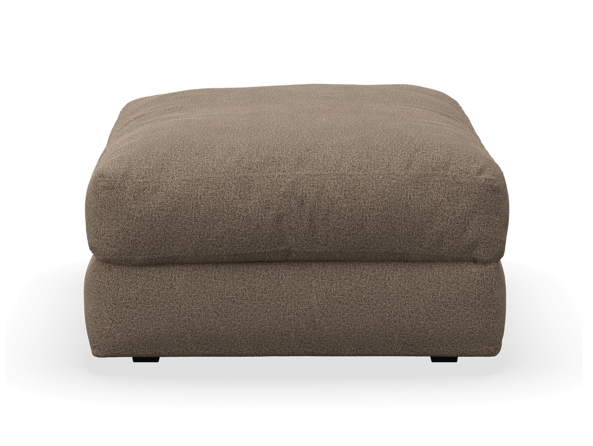 Brun tygklädd ottoman/puff med mjuk rektangulär form sedd framifrån.