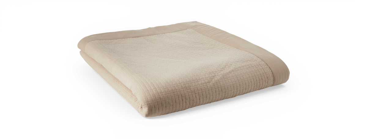 Vikad beige quiltad pläd/överkast med bred kant mot svart bakgrund.