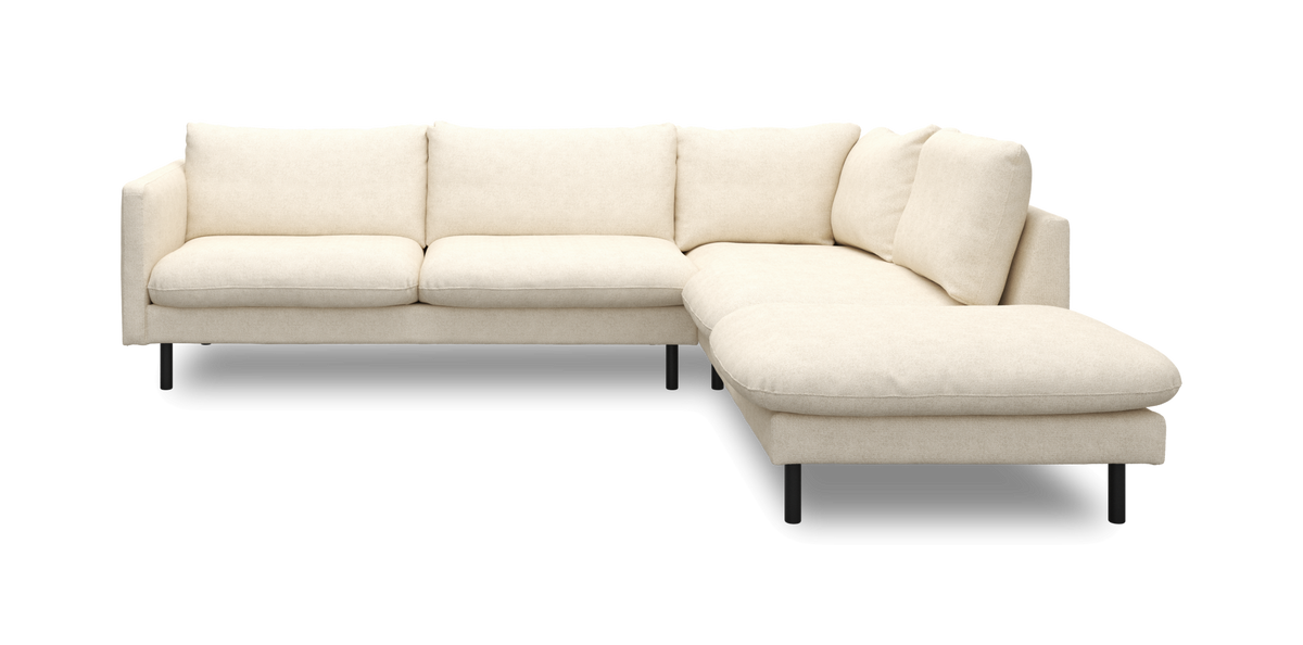 L-formad beige modulsoffa med högerställd schäslong, mjuka kuddar och svarta ben, frilagd på vit bakgrund.