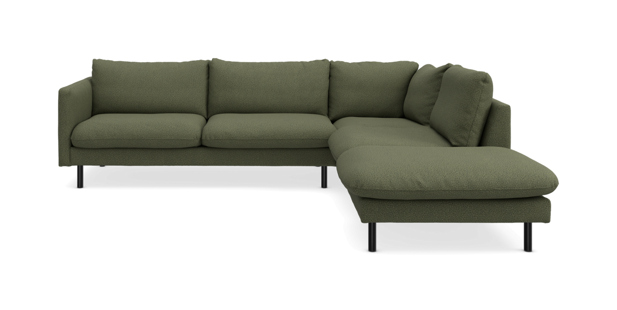 Grön L-formad soffa med schäslong till höger, bouclélik tyg och smala svarta ben, frilagd studiobild.