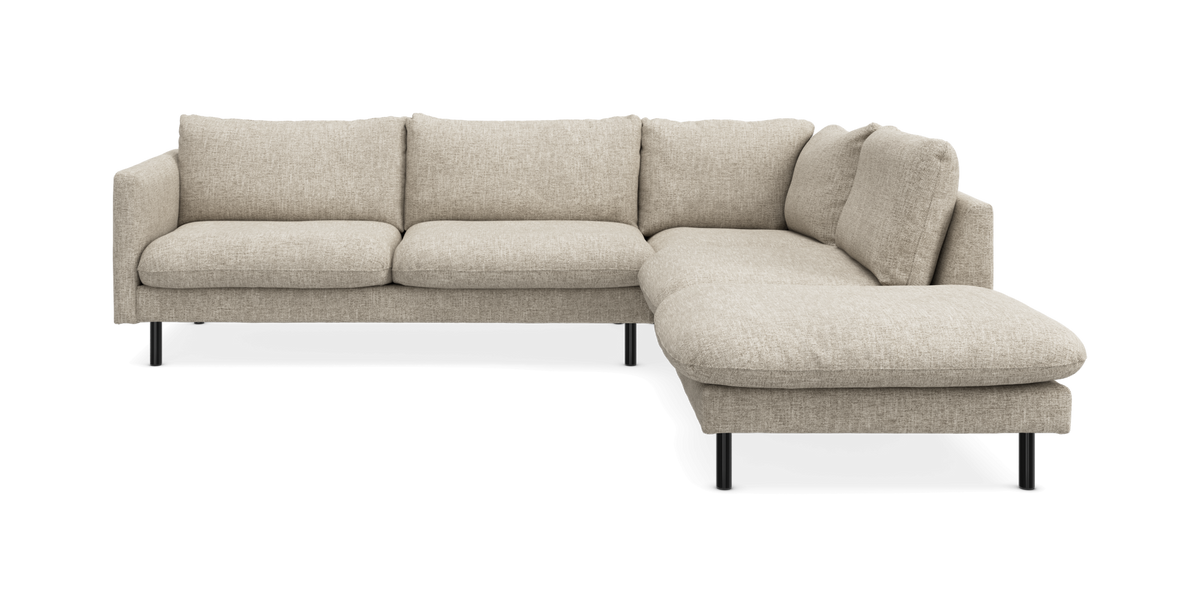 Beige L-formad modulsoffa med schäslong till höger och smala svarta ben, frilagd på vit bakgrund.