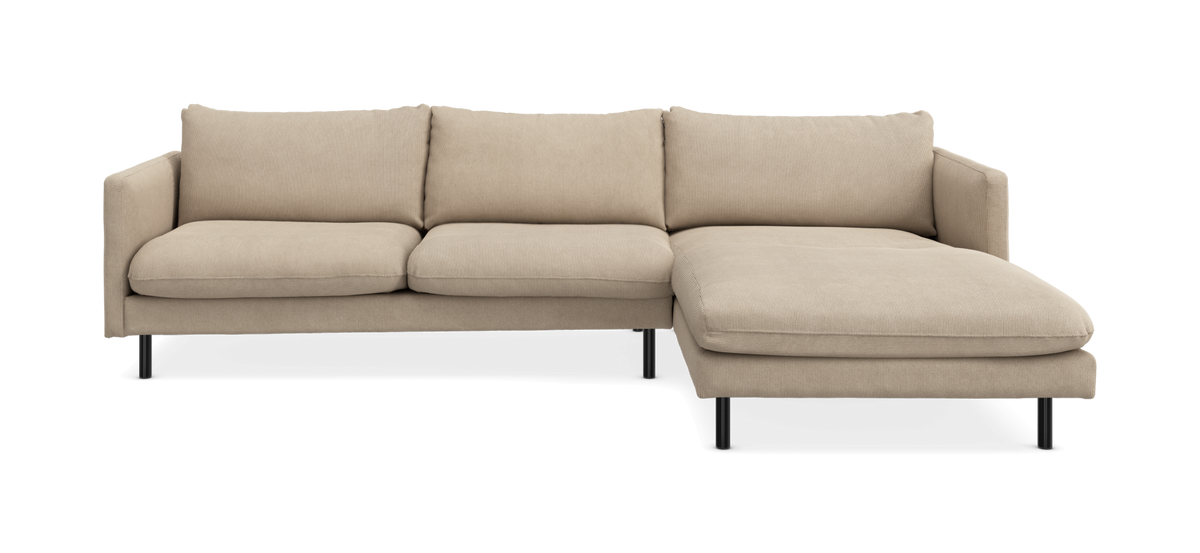 Beige hörnsoffa med divan till höger och slanka svarta ben.