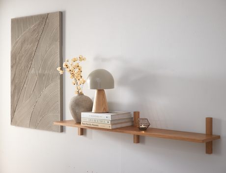 Vägghylla i trä med bordslampa, vas med torkade blommor, ett värmeljus och tre böcker: The Kinfolk Home, Live Beautiful och New Nordic Houses.