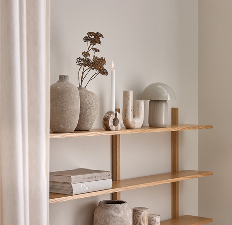 Ljus trähylla med keramikvaser, torkade kvistar, tänt stearinljus, skulpturala stenobjekt, grå svamplampa och böckerna The Kinfolk och Dior i ett ljust, minimalistiskt hem.