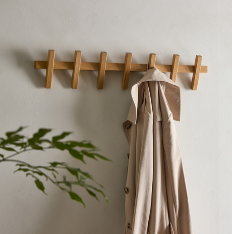 Vägghängd klädkrok i ek med en beige trenchcoat i en ljus, minimalistisk hall.