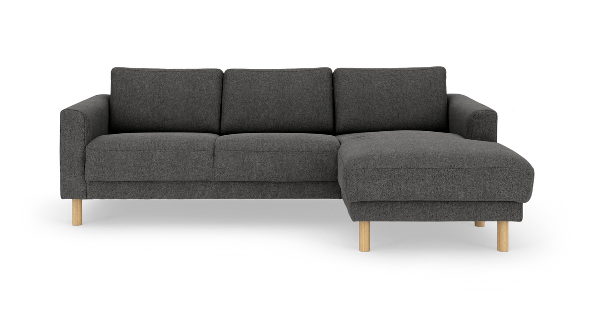 Mörkgrå 3-sits soffa med schäslong till höger och ljusa träben, frilagd på vit bakgrund.