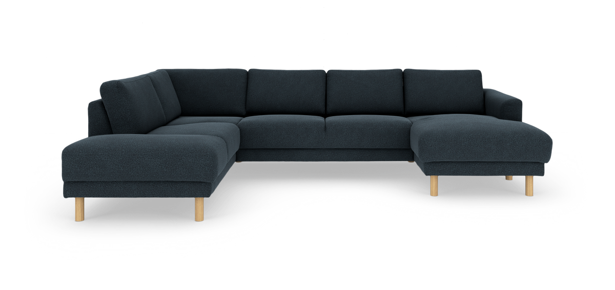 Mörkblå modulsoffa i U‑form med schäslong och ljusa träben, frilagd mot vit bakgrund.