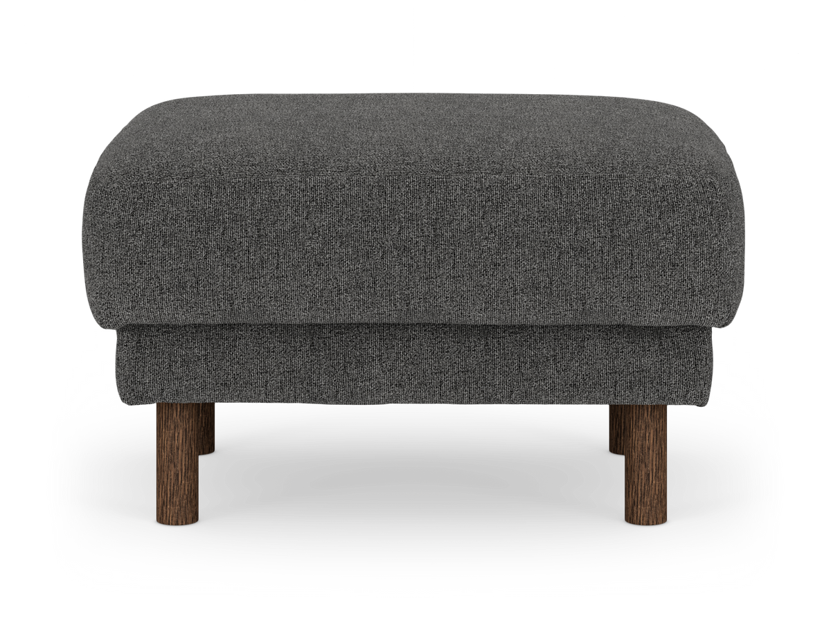 Mörkgrå tygpall/ottoman med runda träben i mörkbrun finish, frilagd på vit bakgrund.