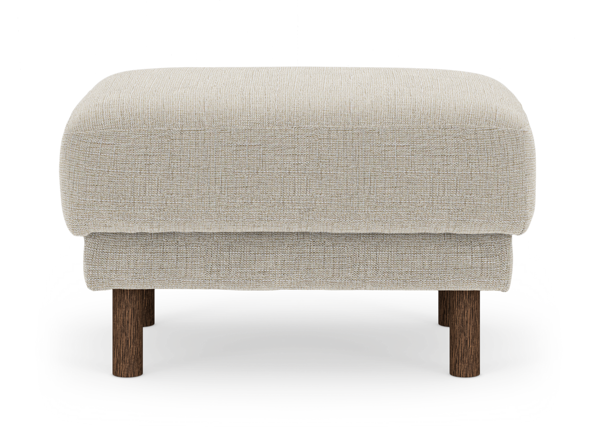 Beige fotpall/ottoman i tyg med runda mörkbruna träben, frilagd på vit bakgrund.