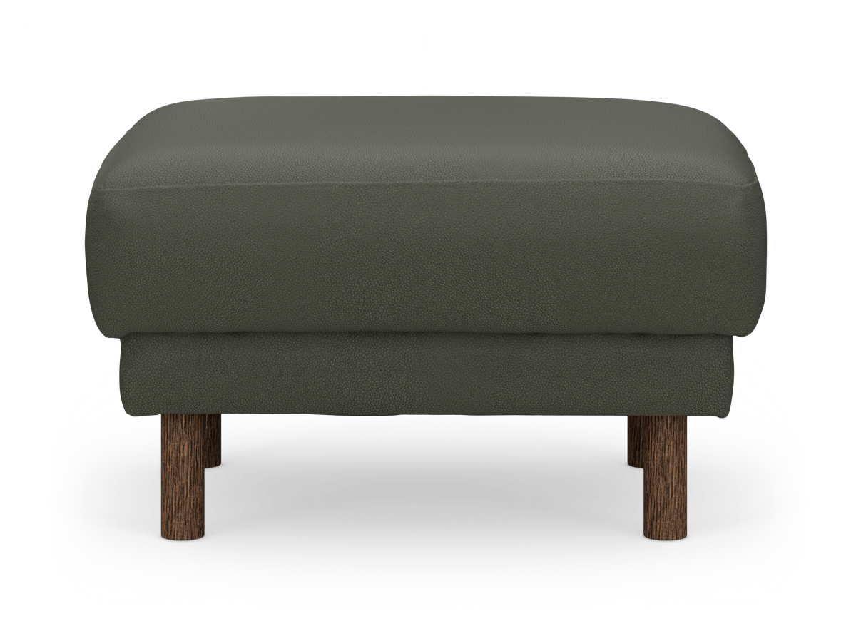 Mörkgrön ottoman/fotpall i läderlook med runda ben i mörkbrunt trä, frontvy på frilagd bakgrund.